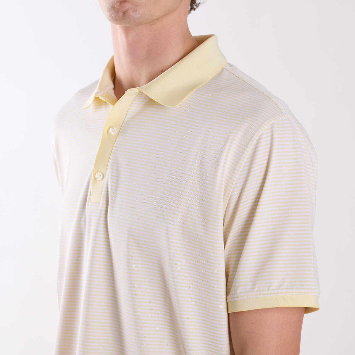 Close-up of COAST micro-stripe performance polo in pale yellow with white stripes, featuring a classic collar and three-button placket.