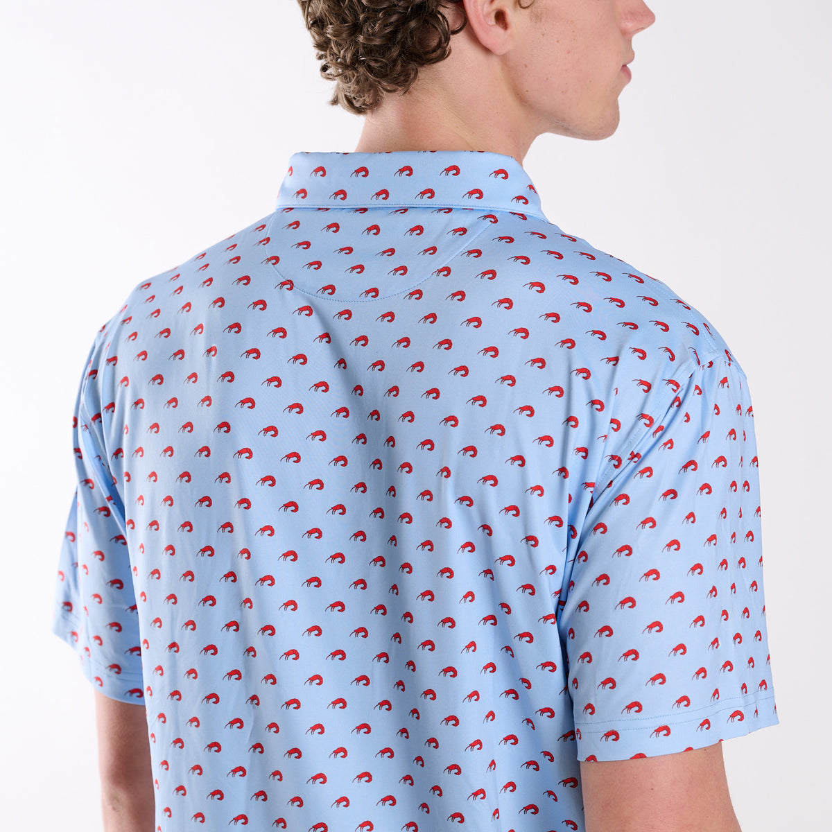 Close-up back detail of light blue polo showing repeating red shrimp pattern and collar.