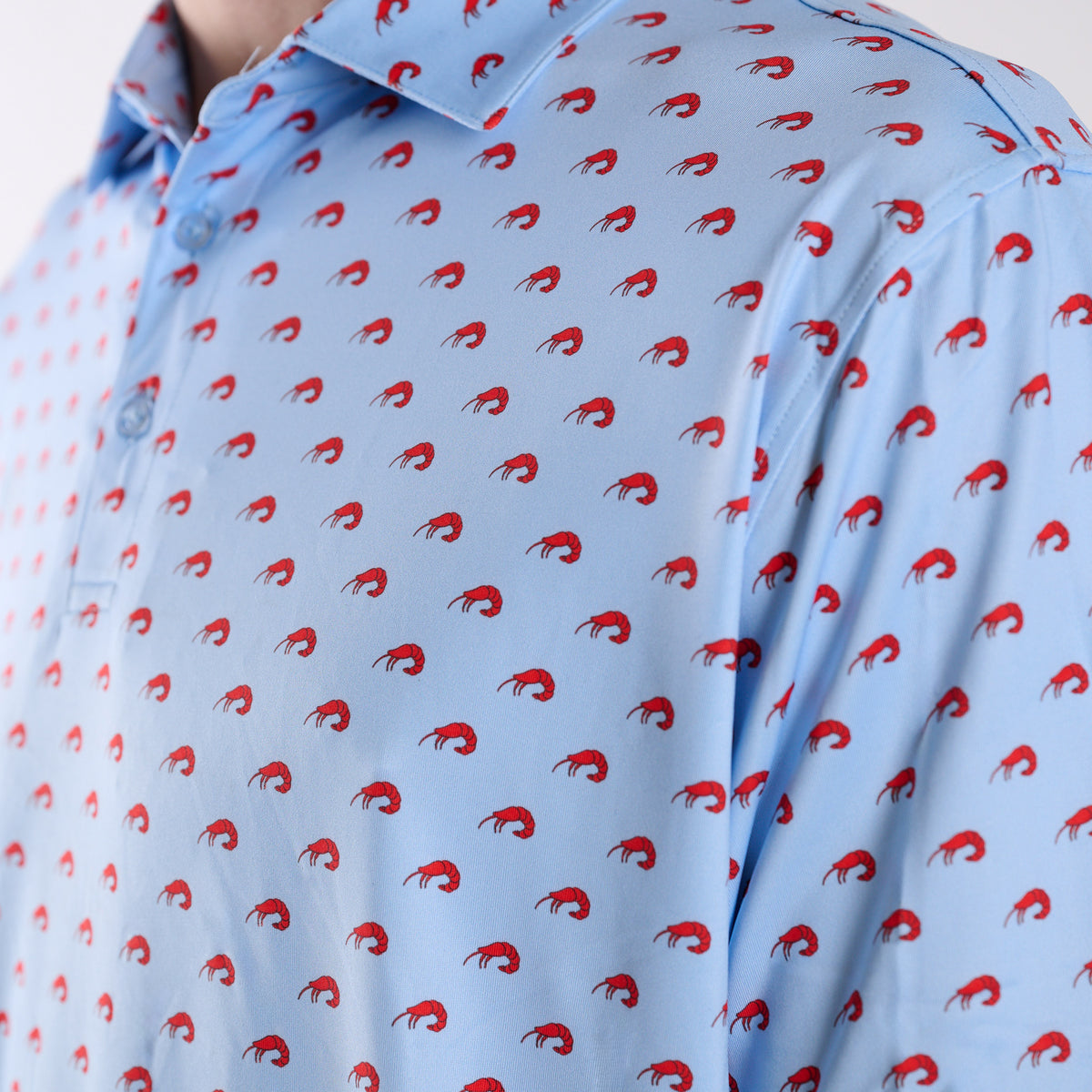 Close-up front detail of light blue polo fabric featuring small red shrimp print pattern.
