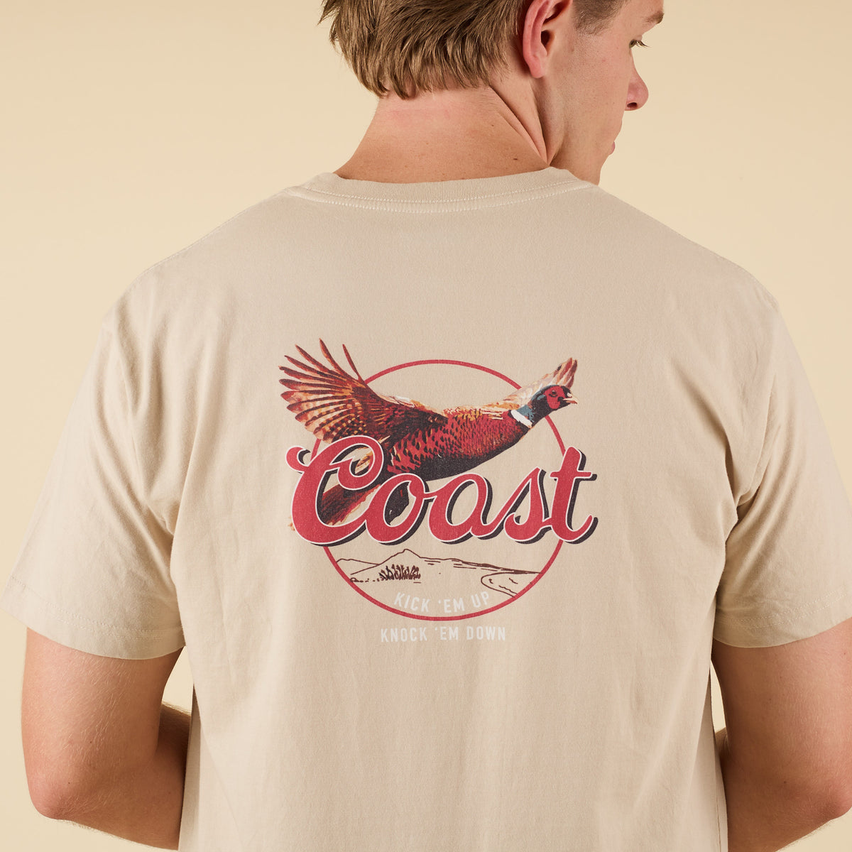 Back view of COAST Pheasant t-shirt featuring a large flying pheasant graphic and Coast lettering with “Kick ’Em Up, Knock ’Em Down” slogan.