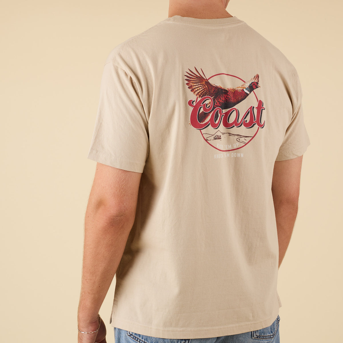 Angled back view of COAST Pheasant beige t-shirt showing bold pheasant graphic design across back.