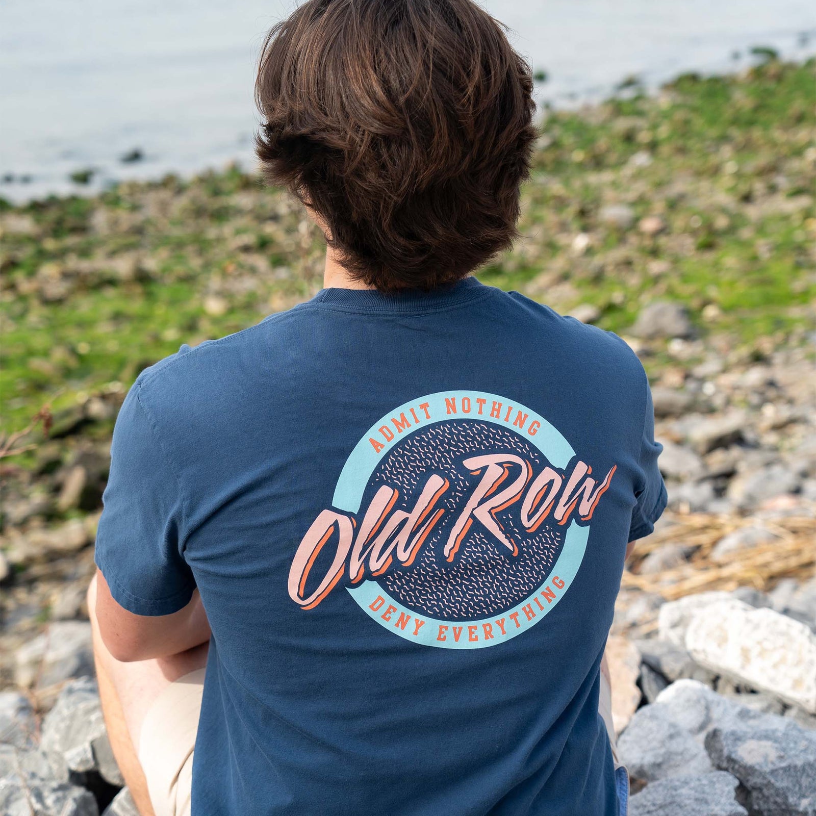 man sitting near a pond wearing an old row t-shirt