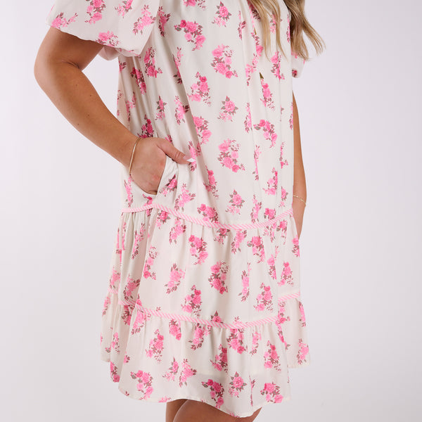 White dress with pink floral pattern worn by a person on a white background
