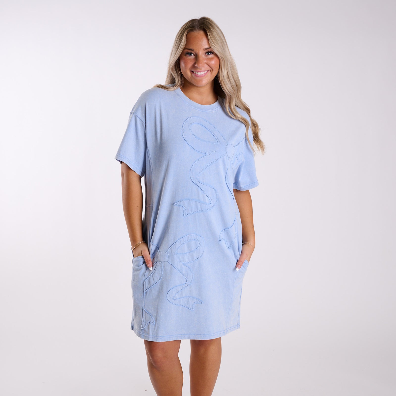 Woman wearing a light blue dress with decorative bow elements on a white background