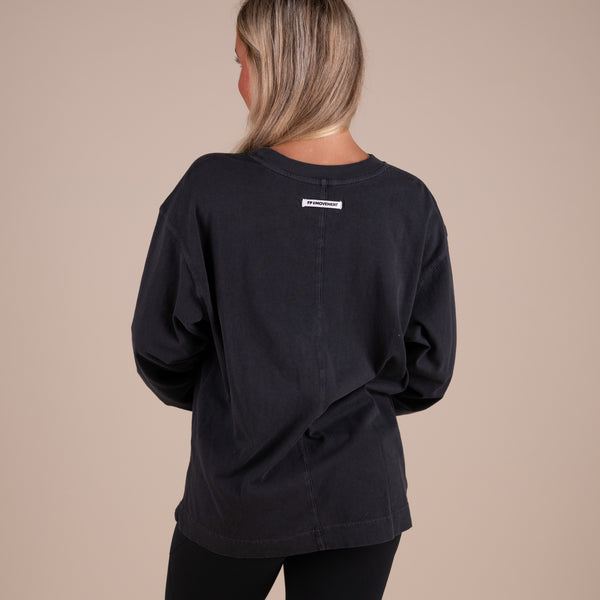 Person wearing a black t-shirt with a visible brand logo on the back against a beige background