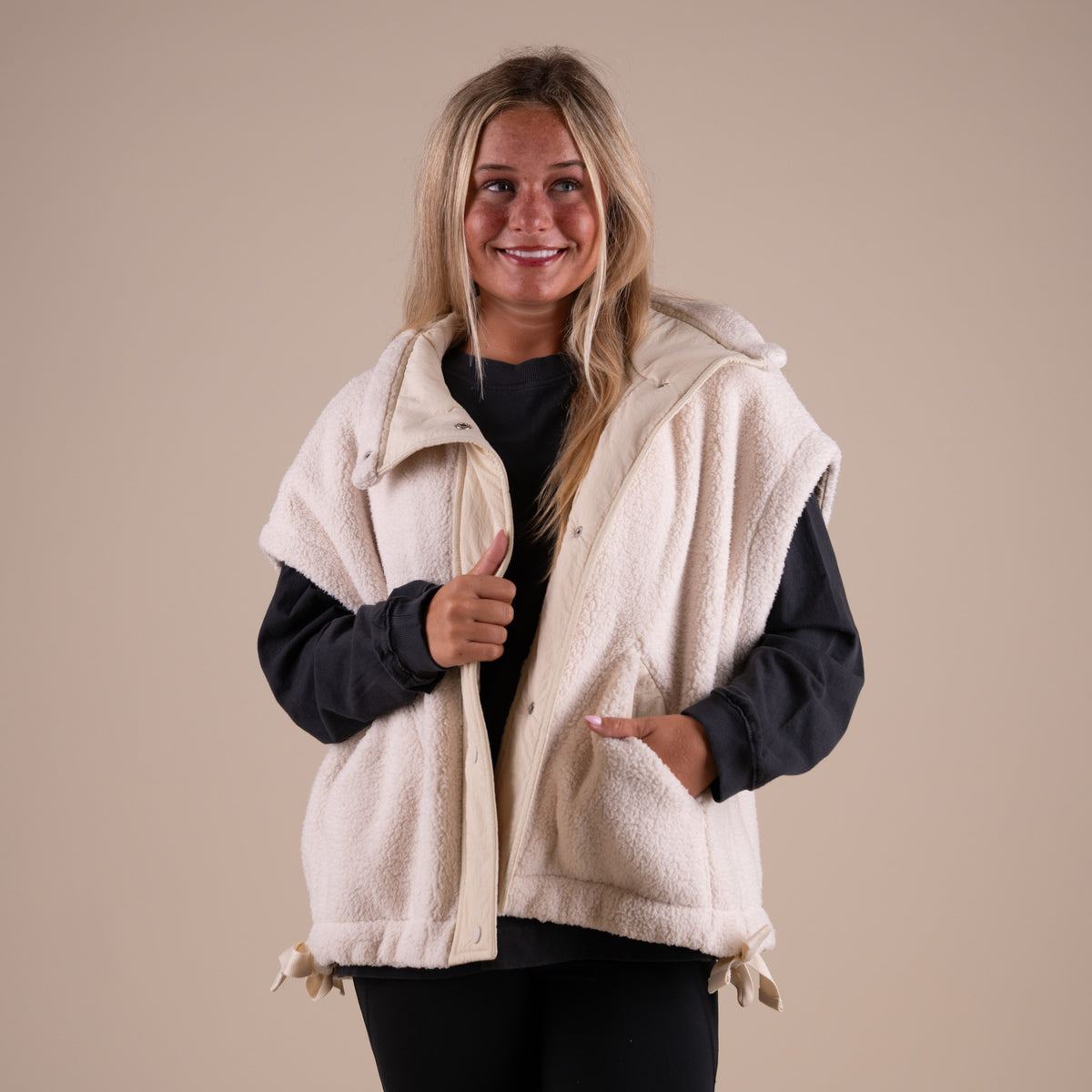 Woman wearing a dark long sleeve shirt under a beige sherpa vest.