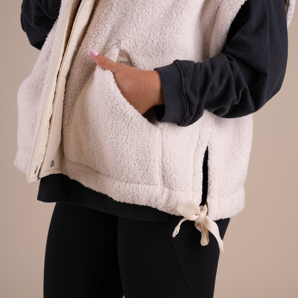 Woman wearing a dark long sleeve shirt under a beige sherpa vest.