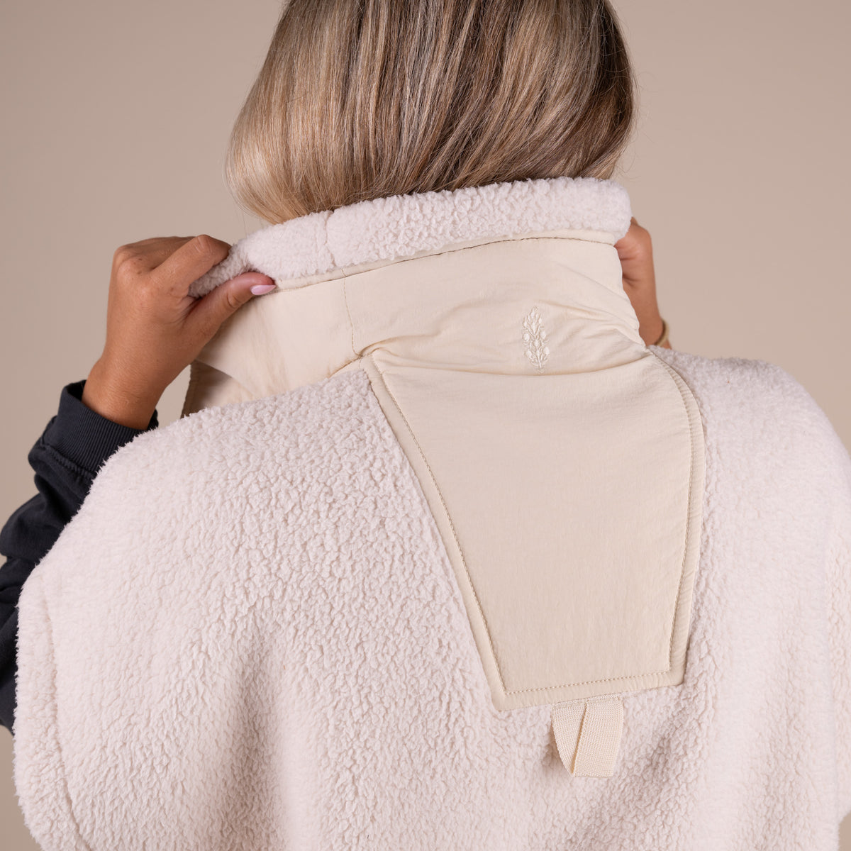 Woman wearing a dark long sleeve shirt under a beige sherpa vest.