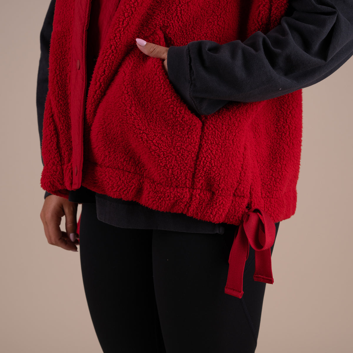 Red fleece vest worn over a black outfit on a beige background