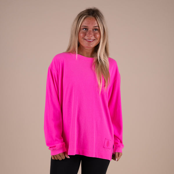 Woman wearing a bright pink long-sleeve shirt against a beige background
