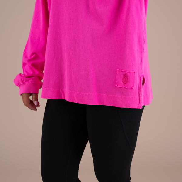 Person wearing a bright pink long-sleeve shirt with a pocket on a beige background
