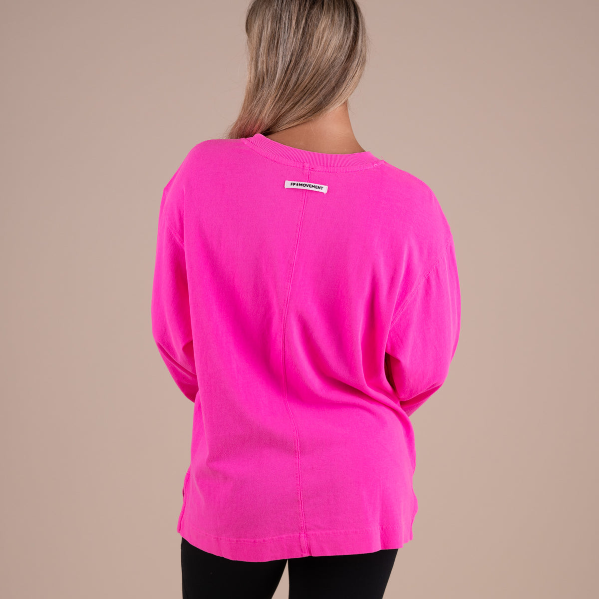 Person wearing a bright pink sweater with a brand label on a beige background
