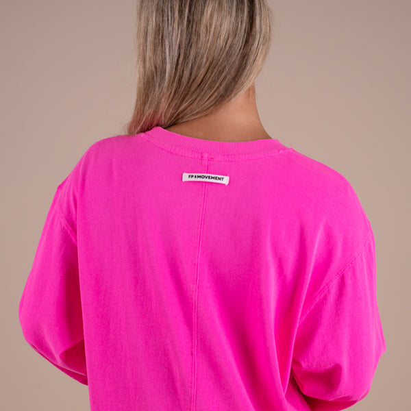 Person wearing a bright pink shirt with a brand label on a beige background