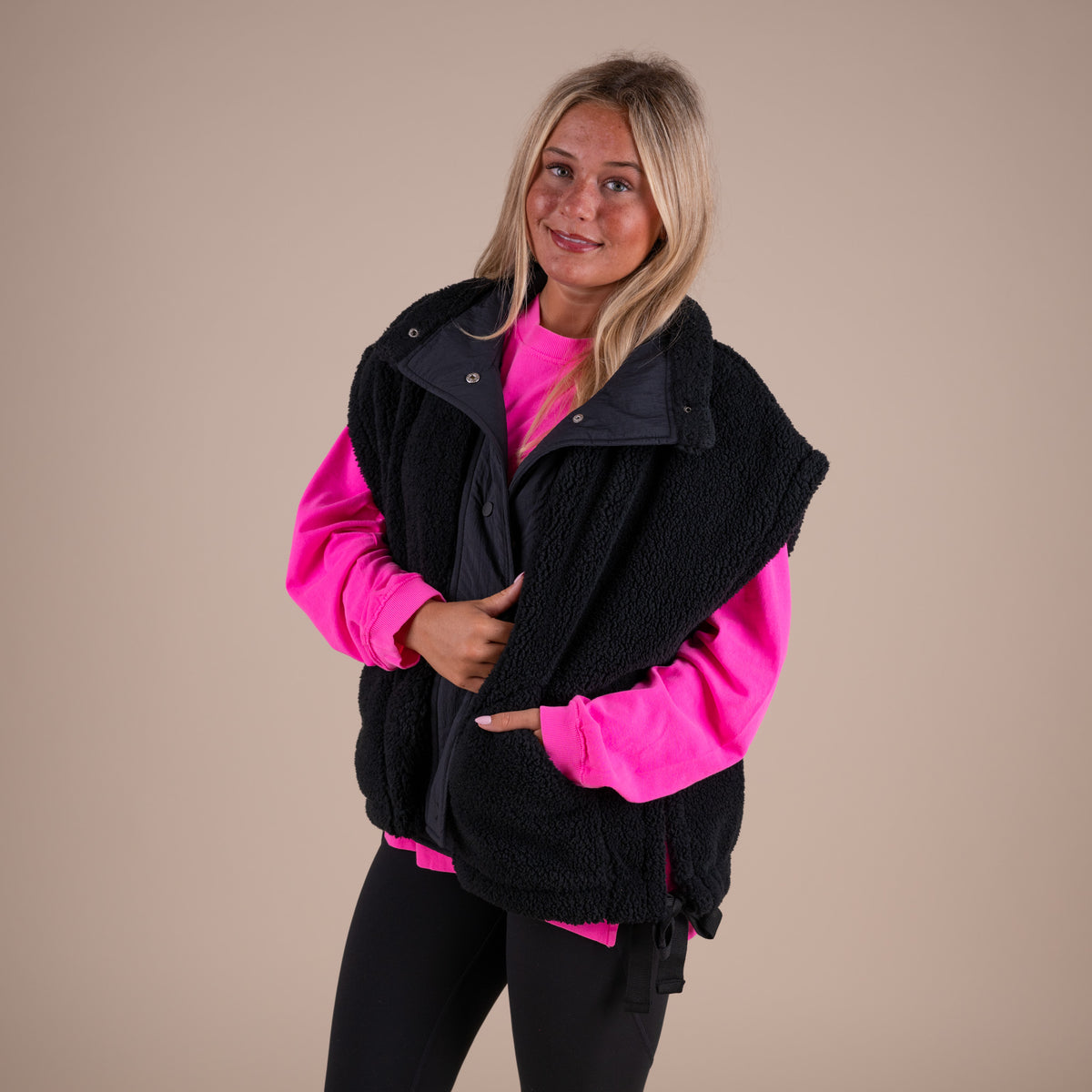 Woman wearing a black vest over a pink shirt on a beige background