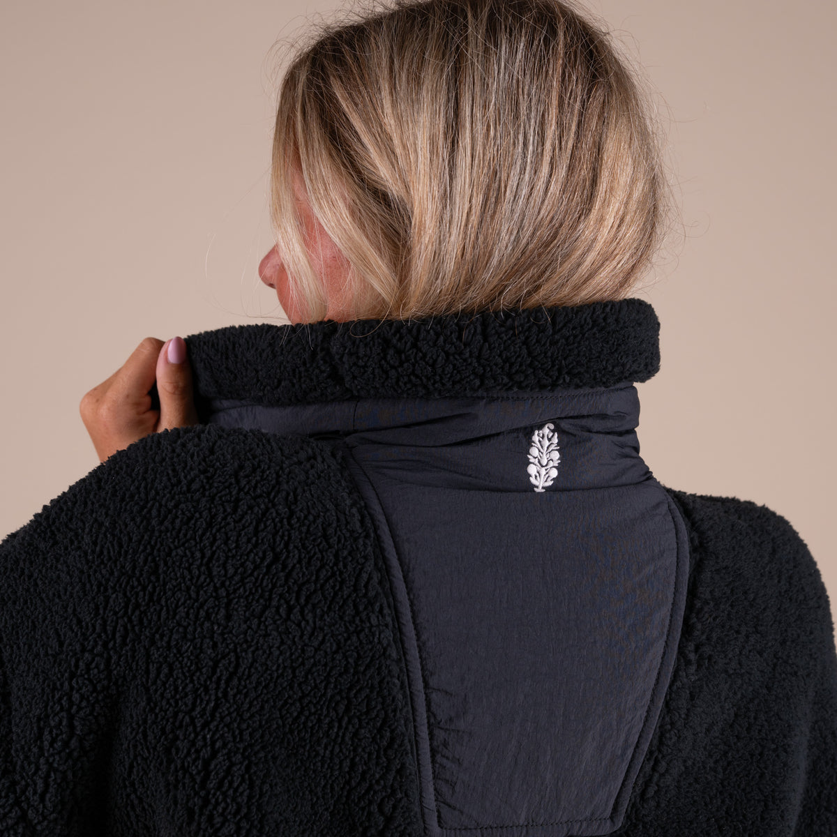 Person wearing a black fleece jacket with a decorative button on a beige background