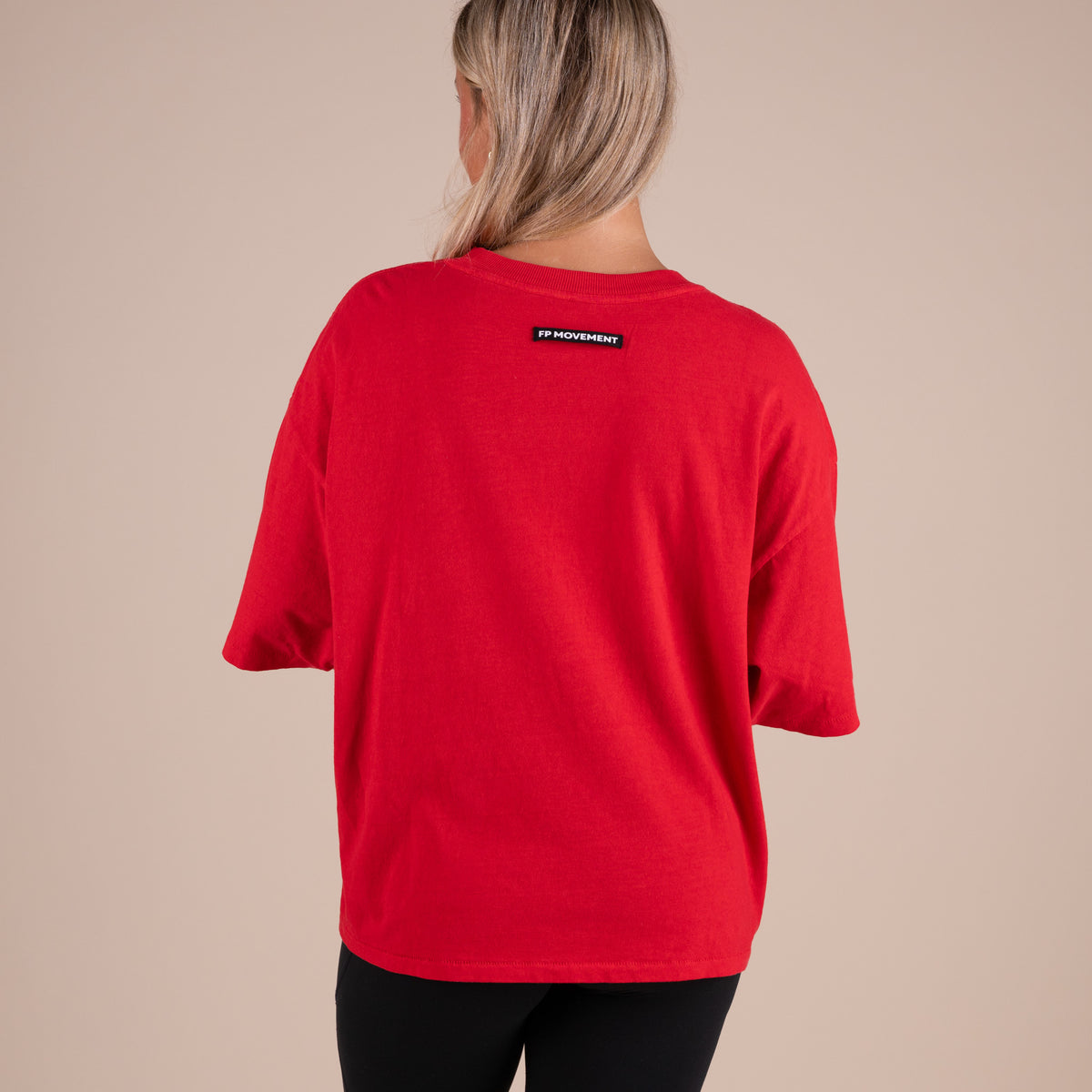 Person wearing a red t-shirt with a logo on the back against a beige background