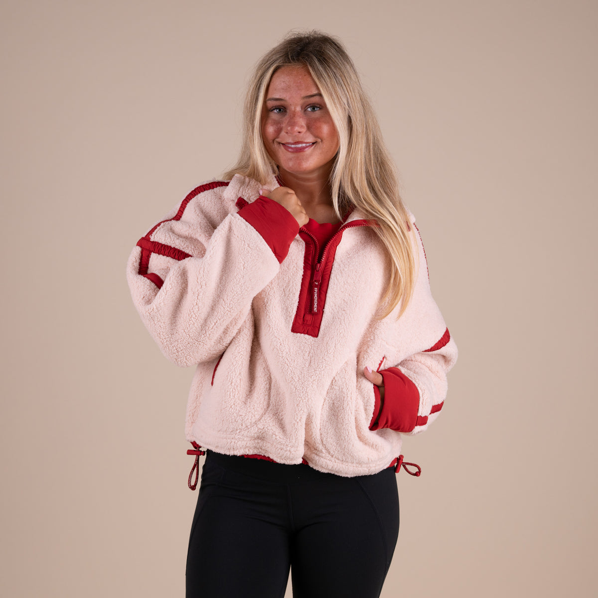 Woman wearing a beige and red fleece jacket on a beige background