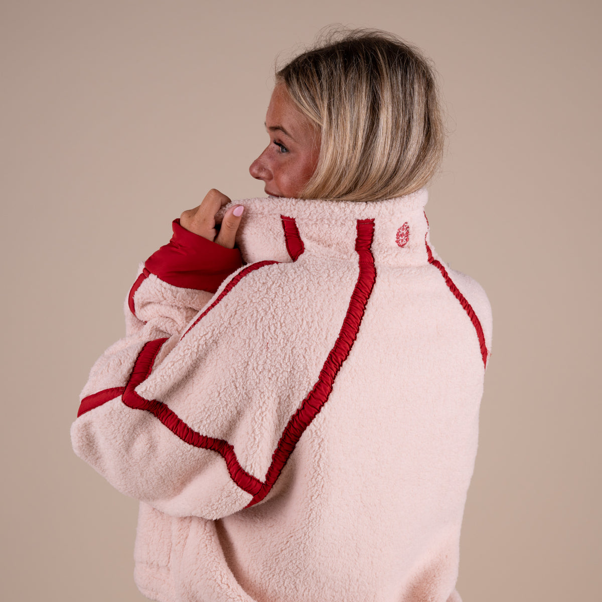 Person wearing a cream fleece jacket with red trim on a beige background