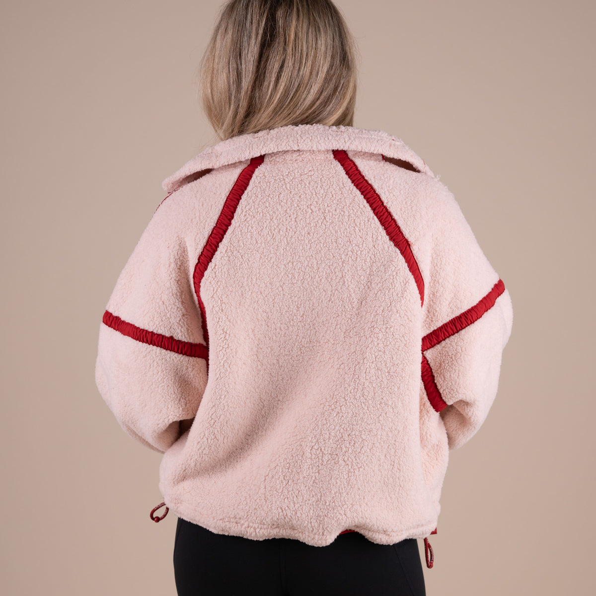 Person wearing a pink fleece jacket with red accents on a beige background
