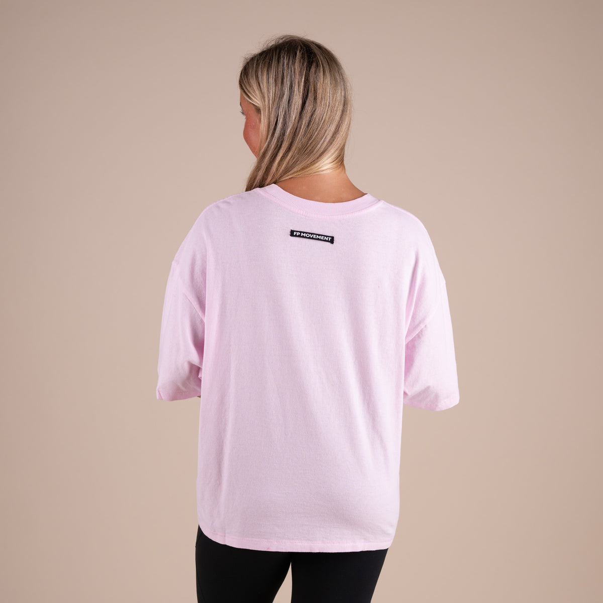 Person wearing a light pink t-shirt with a logo on the back against a beige background