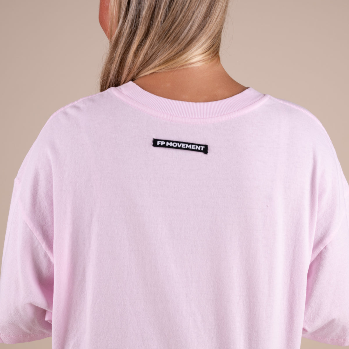 Person wearing a pink t-shirt with 'FP Movement' logo on the back against a beige background