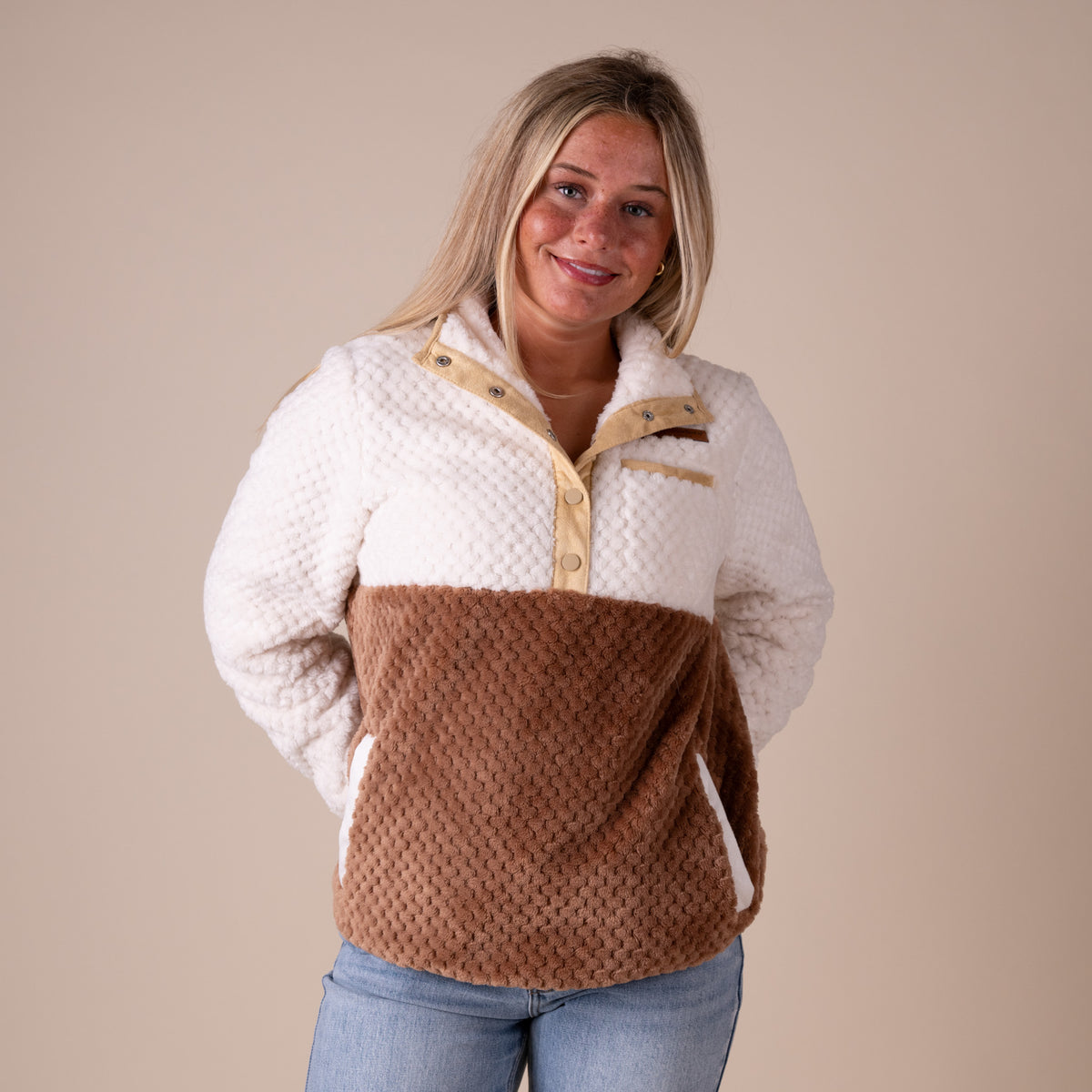 Woman wearing a two-tone fleece pullover with white and brown sections on a beige background