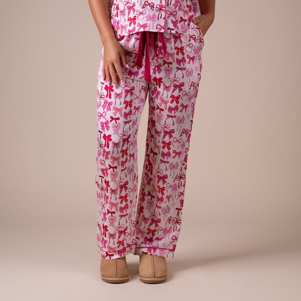 Front view of pink bow print pajama pants featuring velvet drawstring waist and side pockets.