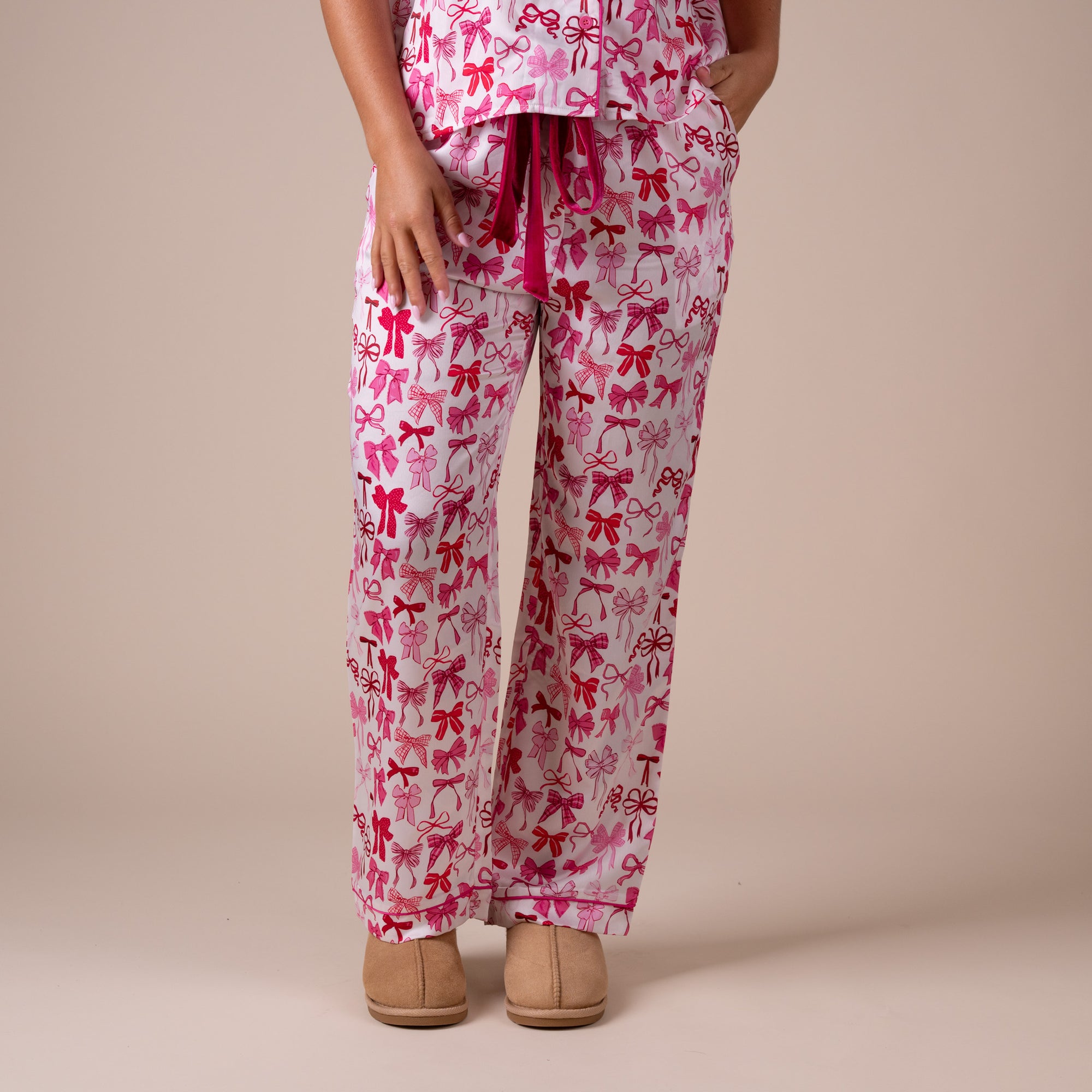 Front view of pink bow print pajama pants featuring velvet drawstring waist and side pockets.