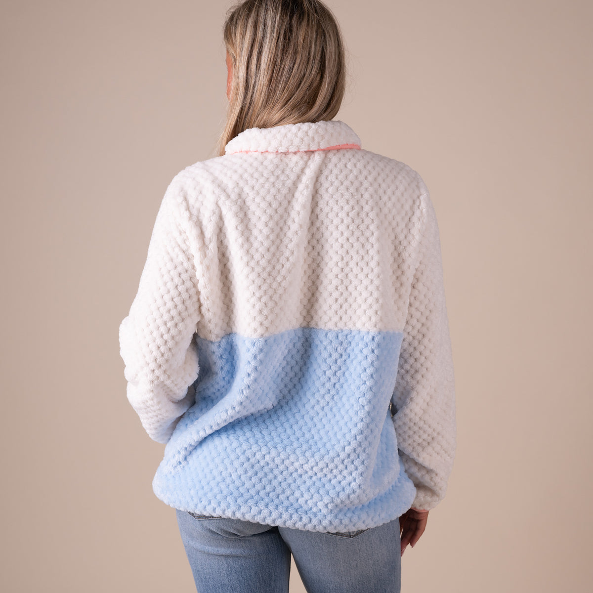 Person wearing a two-tone fleece jacket with beige and light blue sections on a beige background