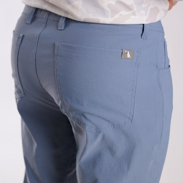 Man wearing Local Boy Outfitters Commuter Pants 2.0 in Steel Blue in front of a white background.