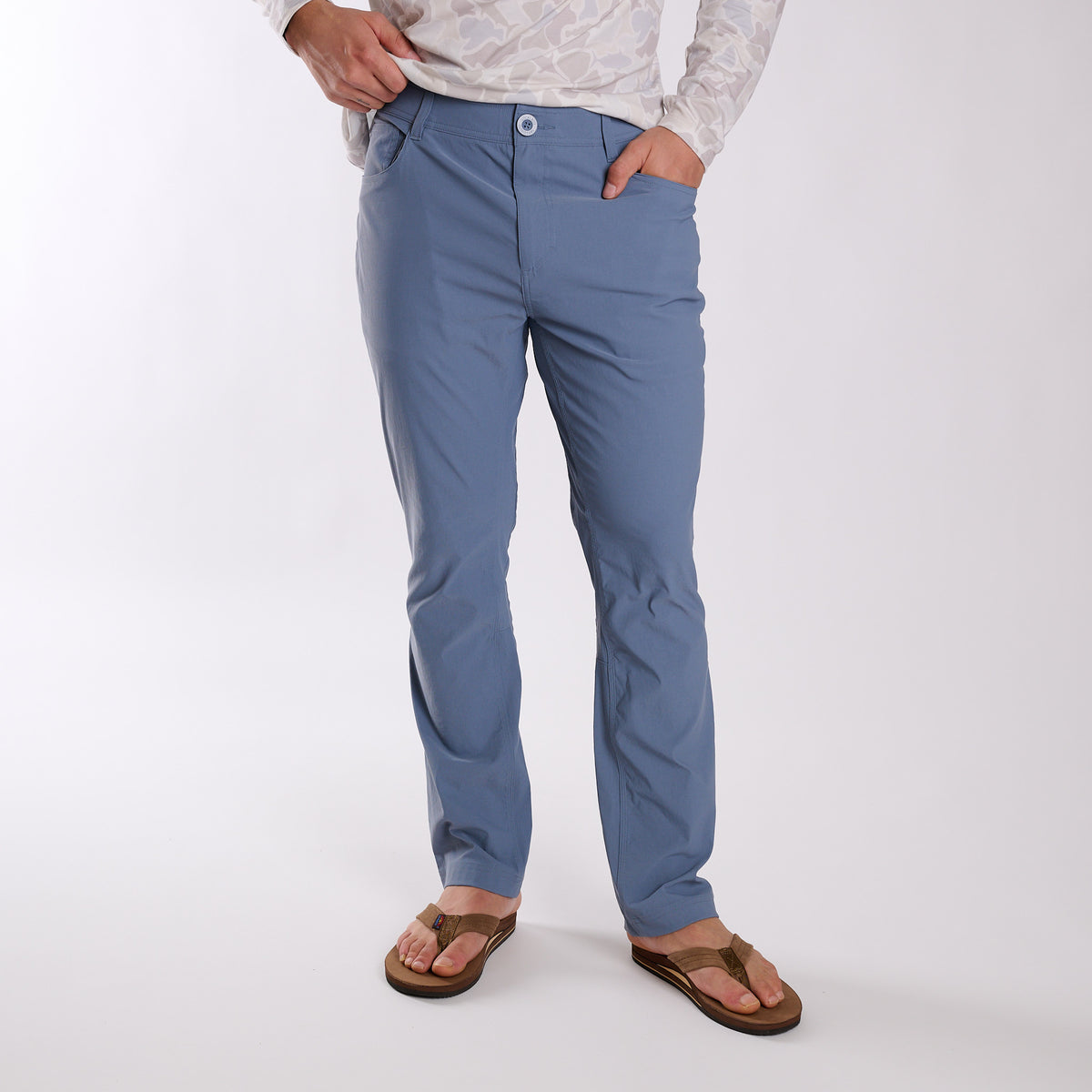 Man wearing Local Boy Outfitters Commuter Pants 2.0 in Steel Blue in front of a white background.
