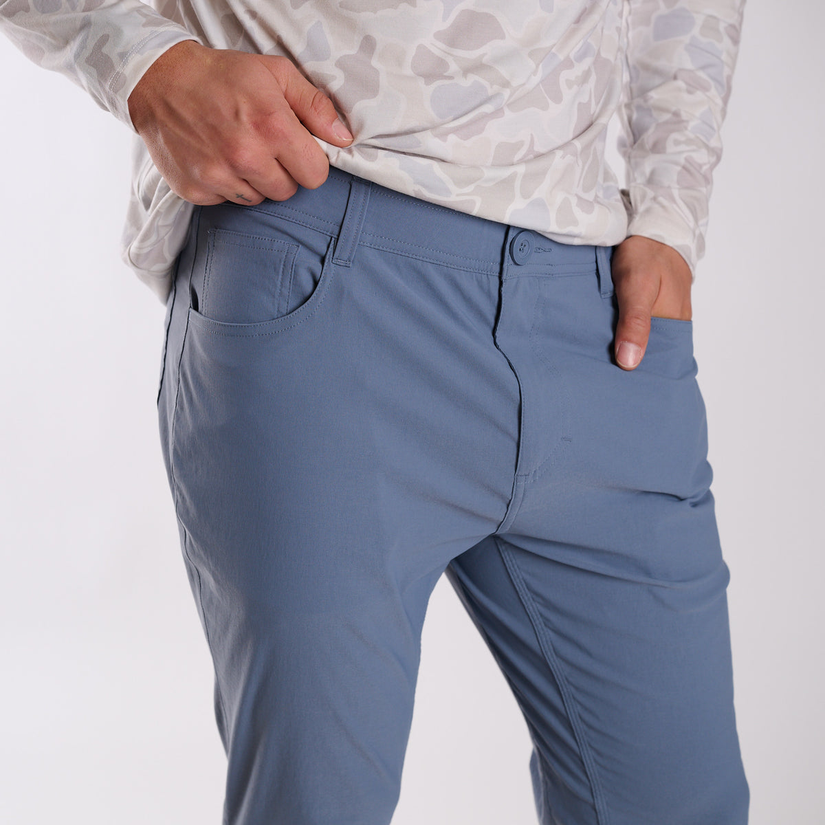 Man wearing Local Boy Outfitters Commuter Pants 2.0 in Steel Blue in front of a white background.