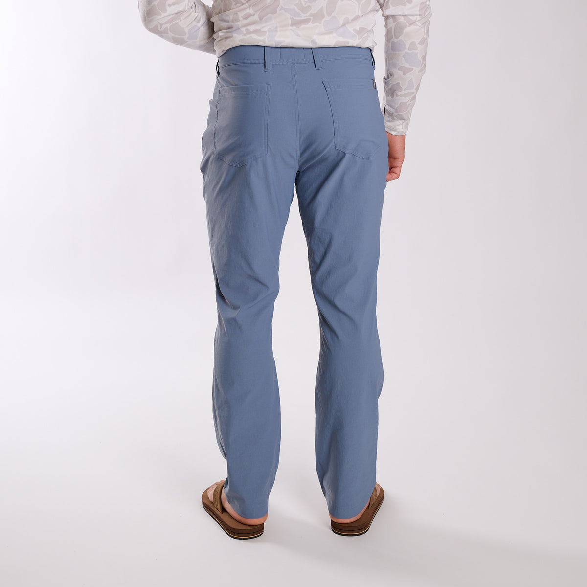 Man wearing Local Boy Outfitters Commuter Pants 2.0 in Steel Blue in front of a white background.