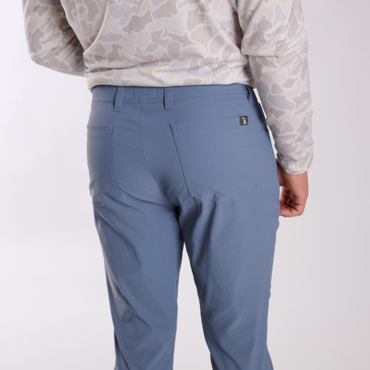Man wearing Local Boy Outfitters Commuter Pants 2.0 in Steel Blue in front of a white background.