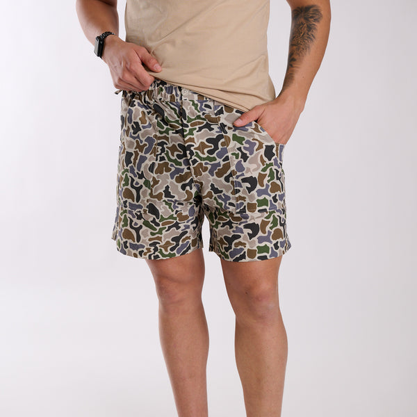 Man wearing local boy outfitters 6 Inch Chum Shorts in Localflage camo in front of a white background