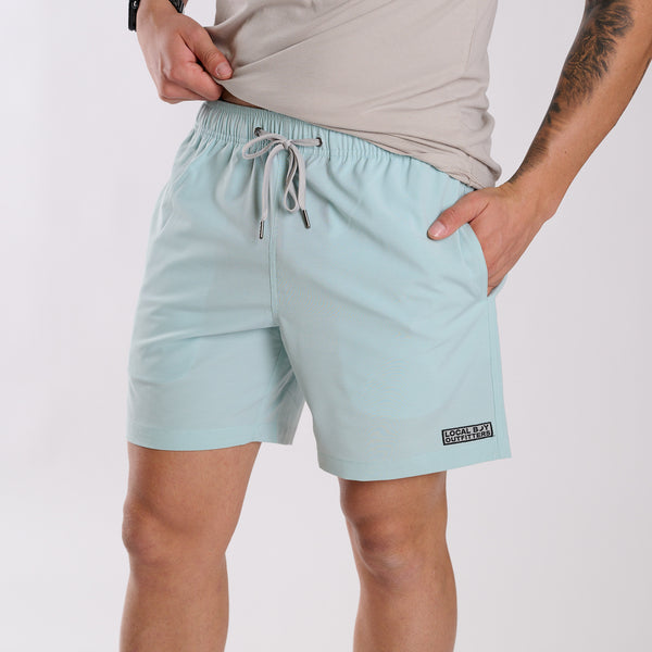 Man wearing Local Boy Outfitters Bayview Swim Trunks in Mint in front of a white backdrop.