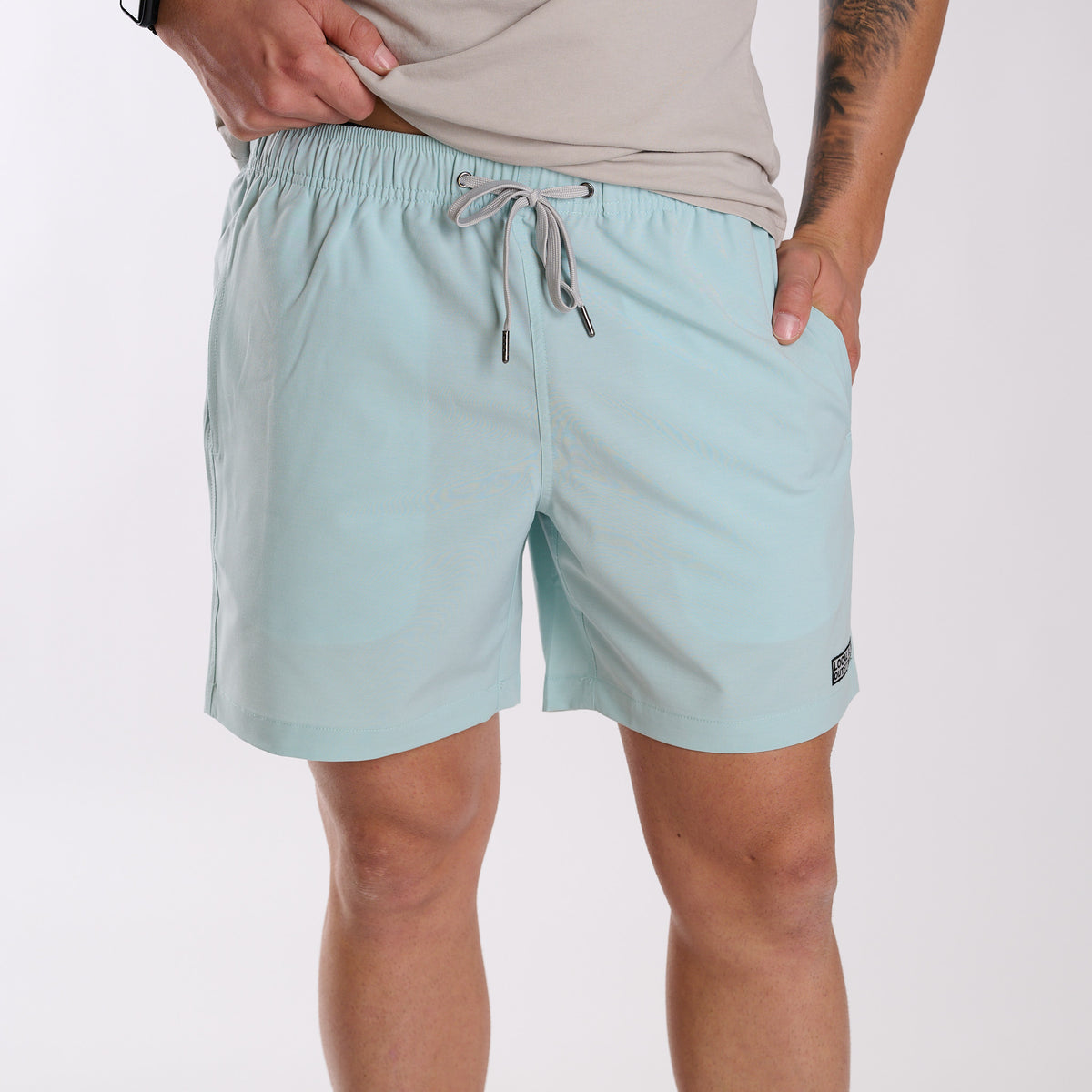 Man wearing Local Boy Outfitters Bayview Swim Trunks in Mint in front of a white backdrop.