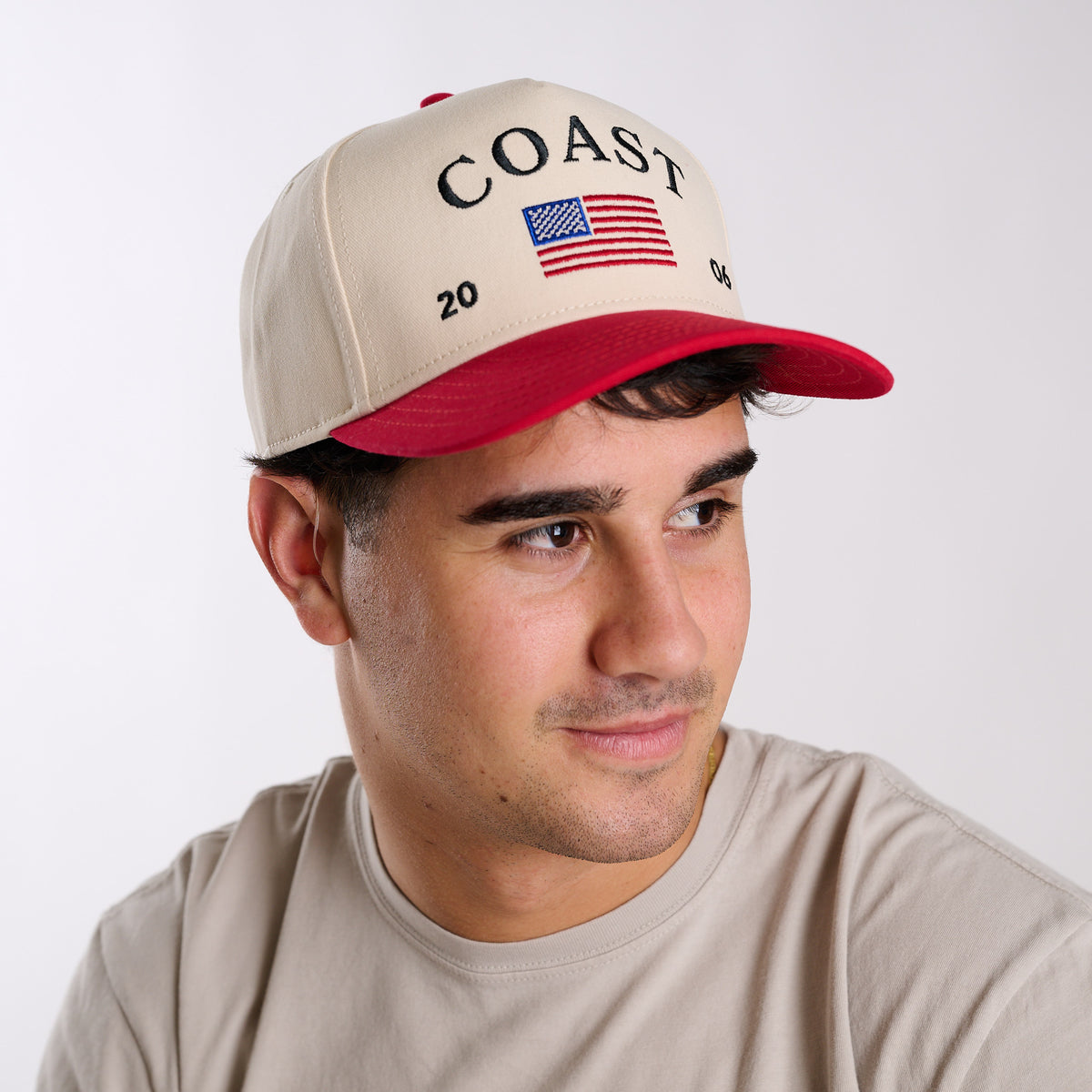 Man wearing a beige and red cap with 'COAST' and an American flag design on a white background