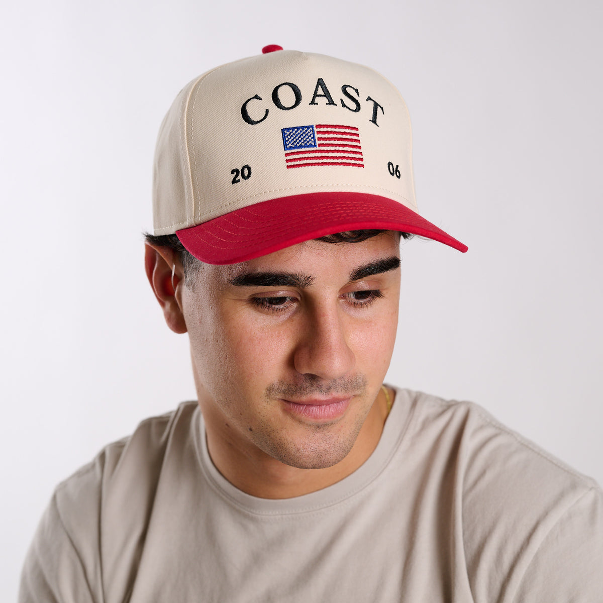 Cream and red trucker hat with “COAST” embroidery and American flag design, front angled view on model