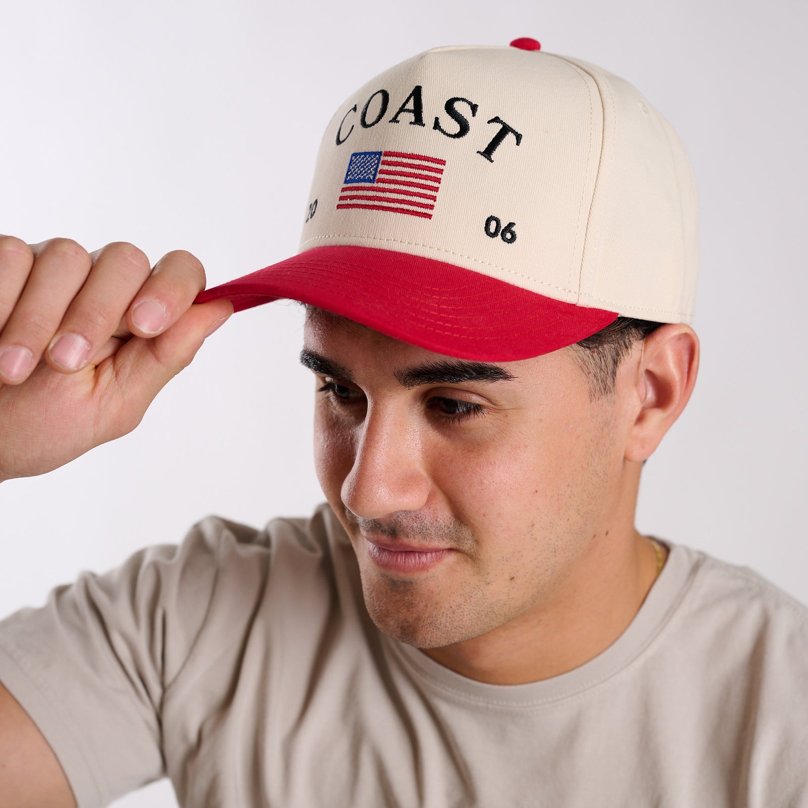 COAST USA trucker hat with red brim and embroidered flag, side view on model adjusting brim