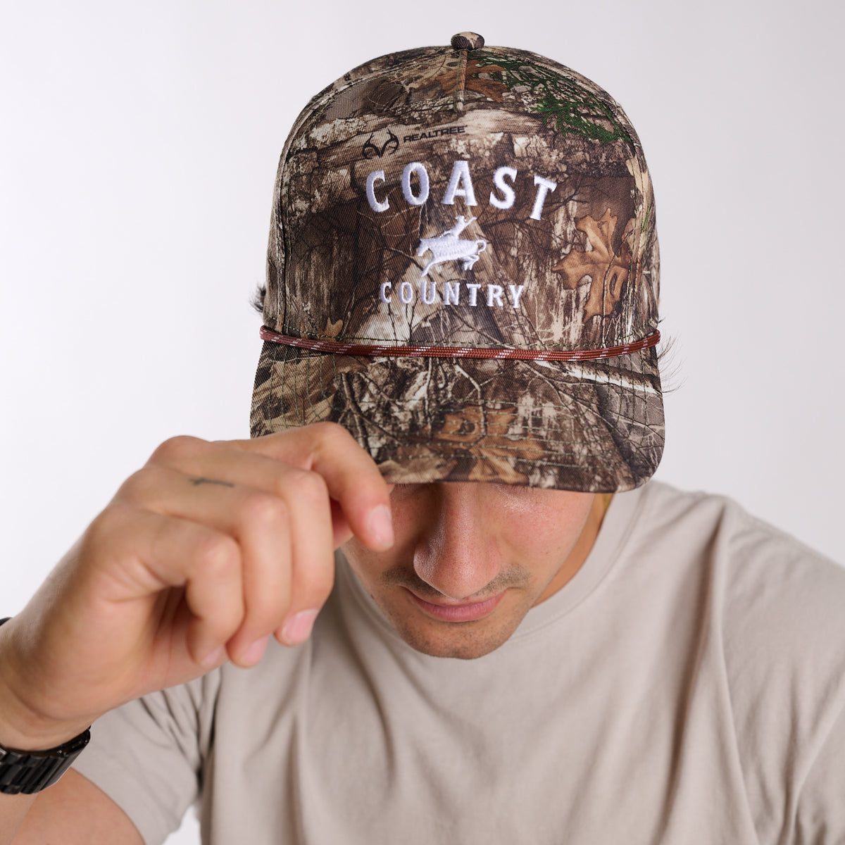 Person wearing a camouflage cap with 'Coast Country' branding on a white background