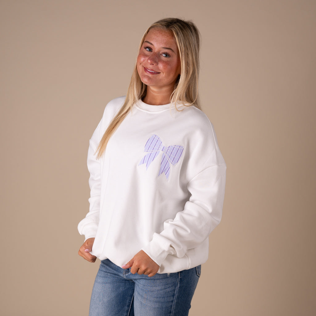 White crewneck sweatshirt with large lavender striped bow graphic on back and small matching bow on front.