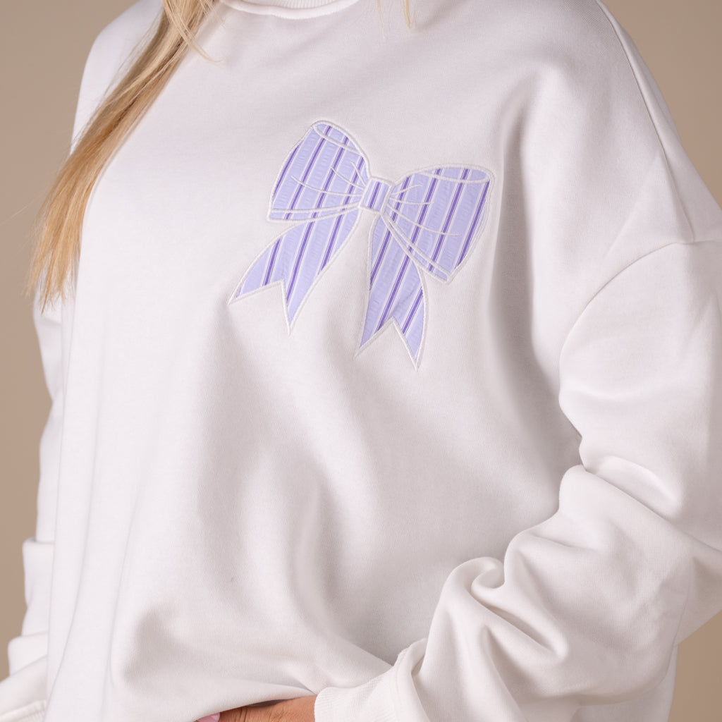 White crewneck sweatshirt with large lavender striped bow graphic on back and small matching bow on front.
