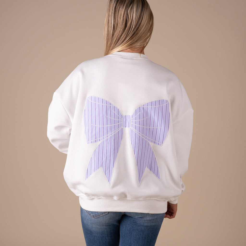 White crewneck sweatshirt with large lavender striped bow graphic on back and small matching bow on front.
