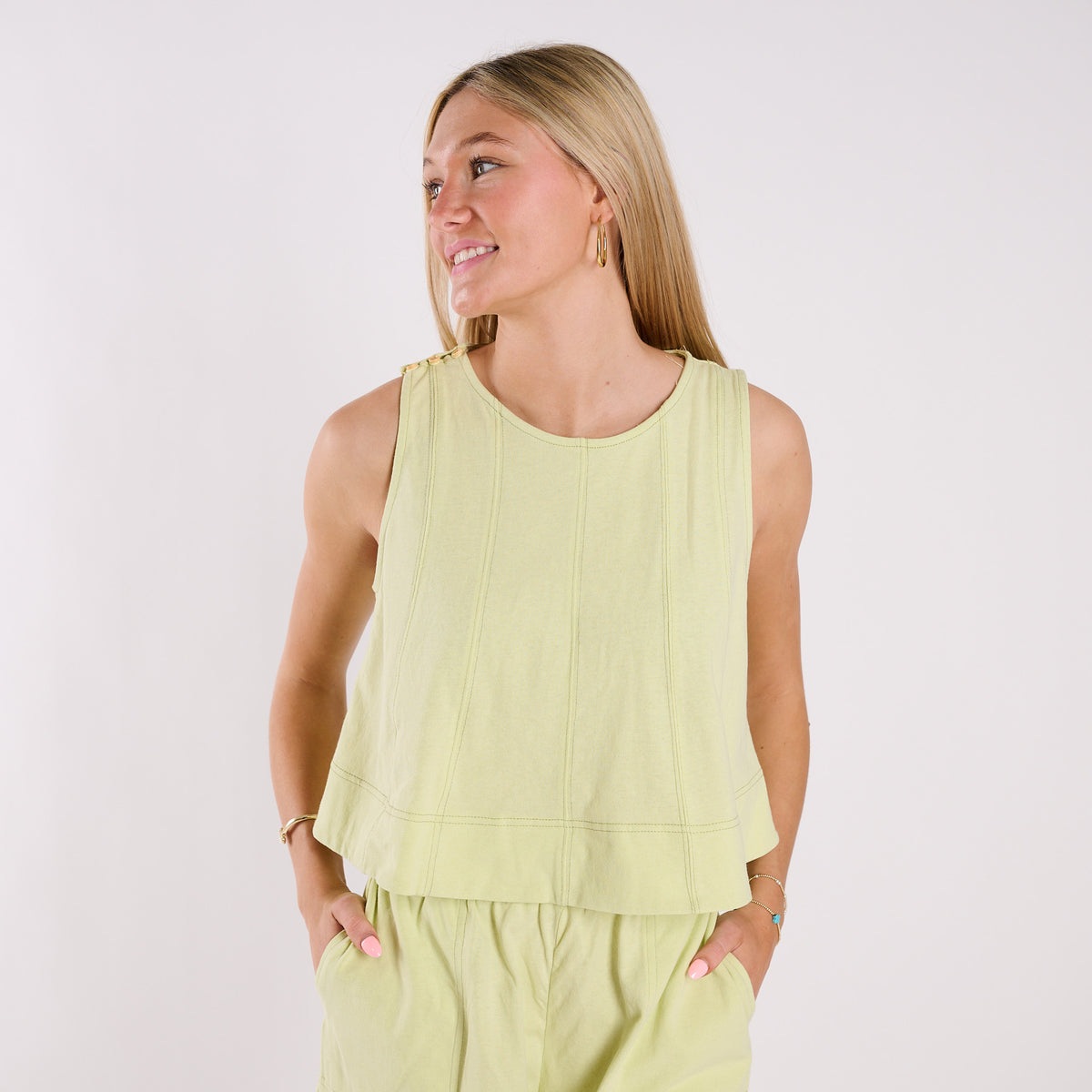 Woman wearing a light green sleeveless top and pants against a white background