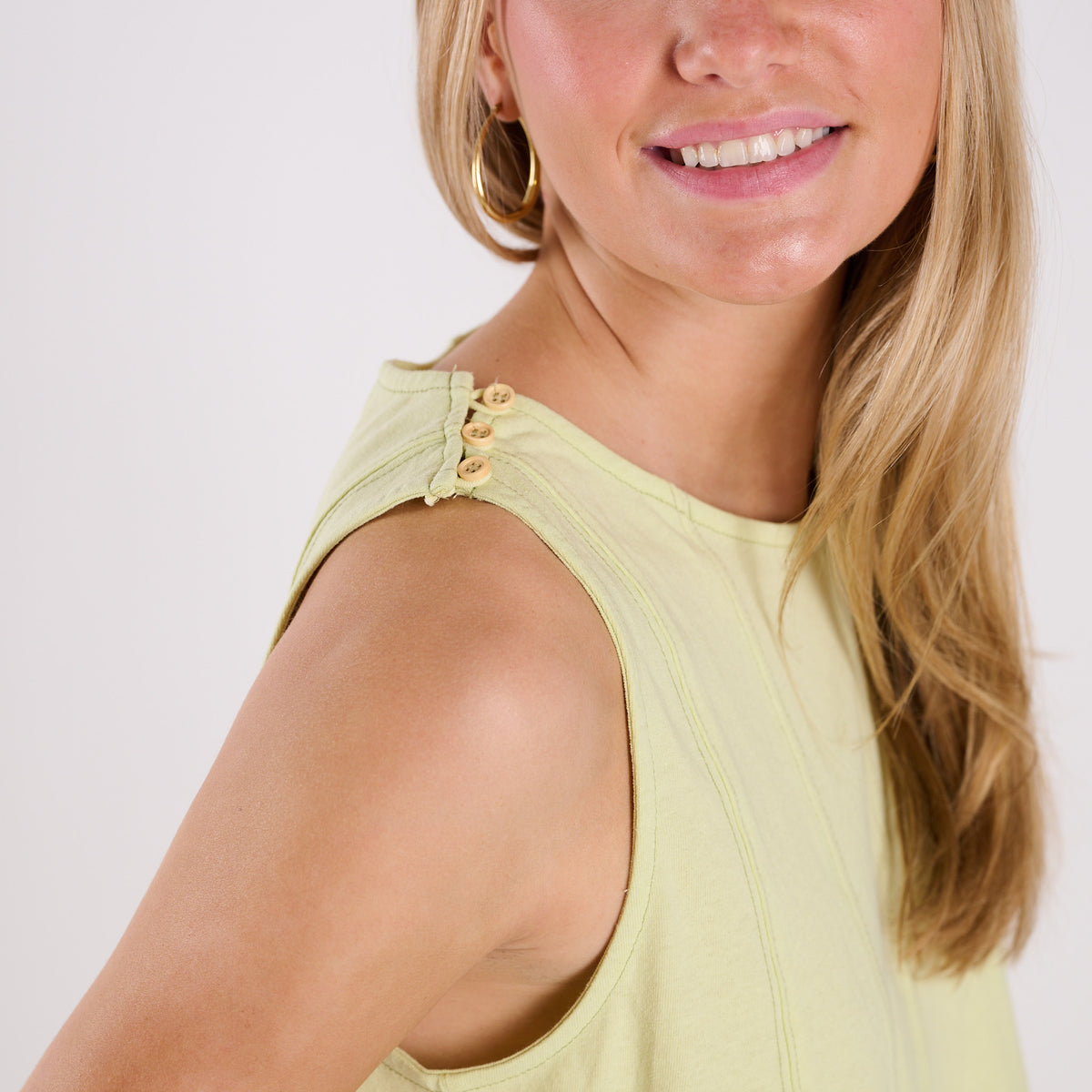 Woman wearing a light green sleeveless top with a plain background