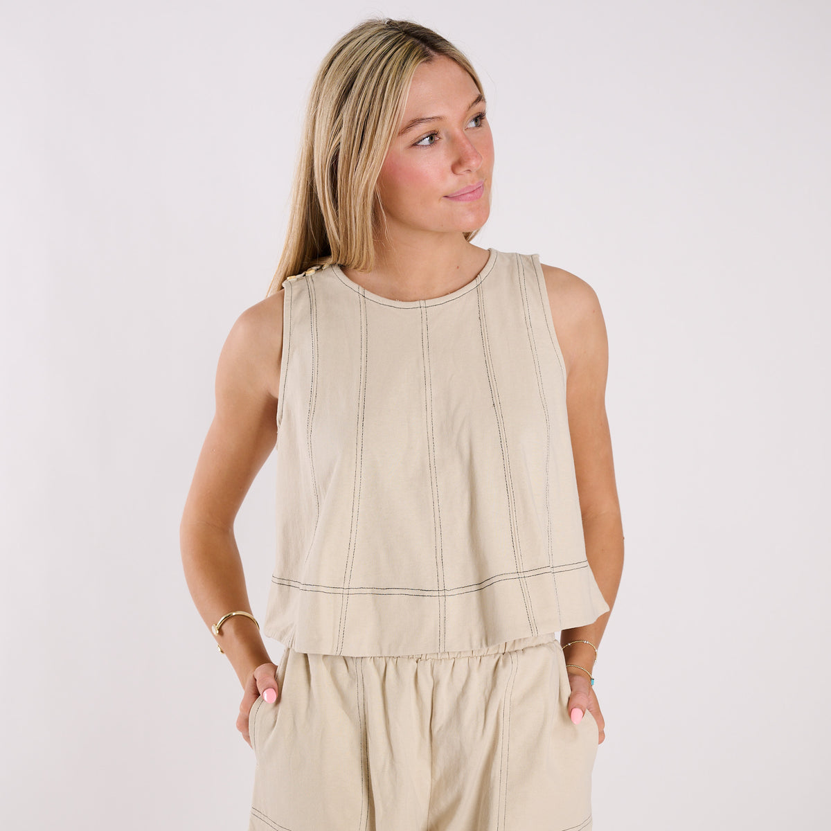 Woman wearing a beige sleeveless top and pants on a white background