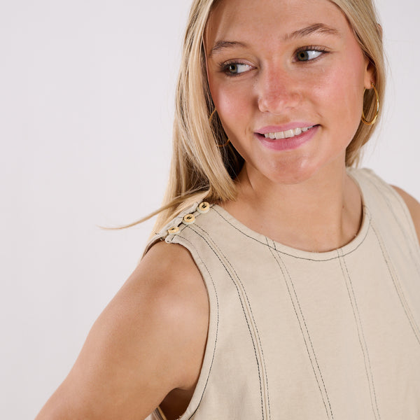  Woman wearing a beige sleeveless top against a plain background