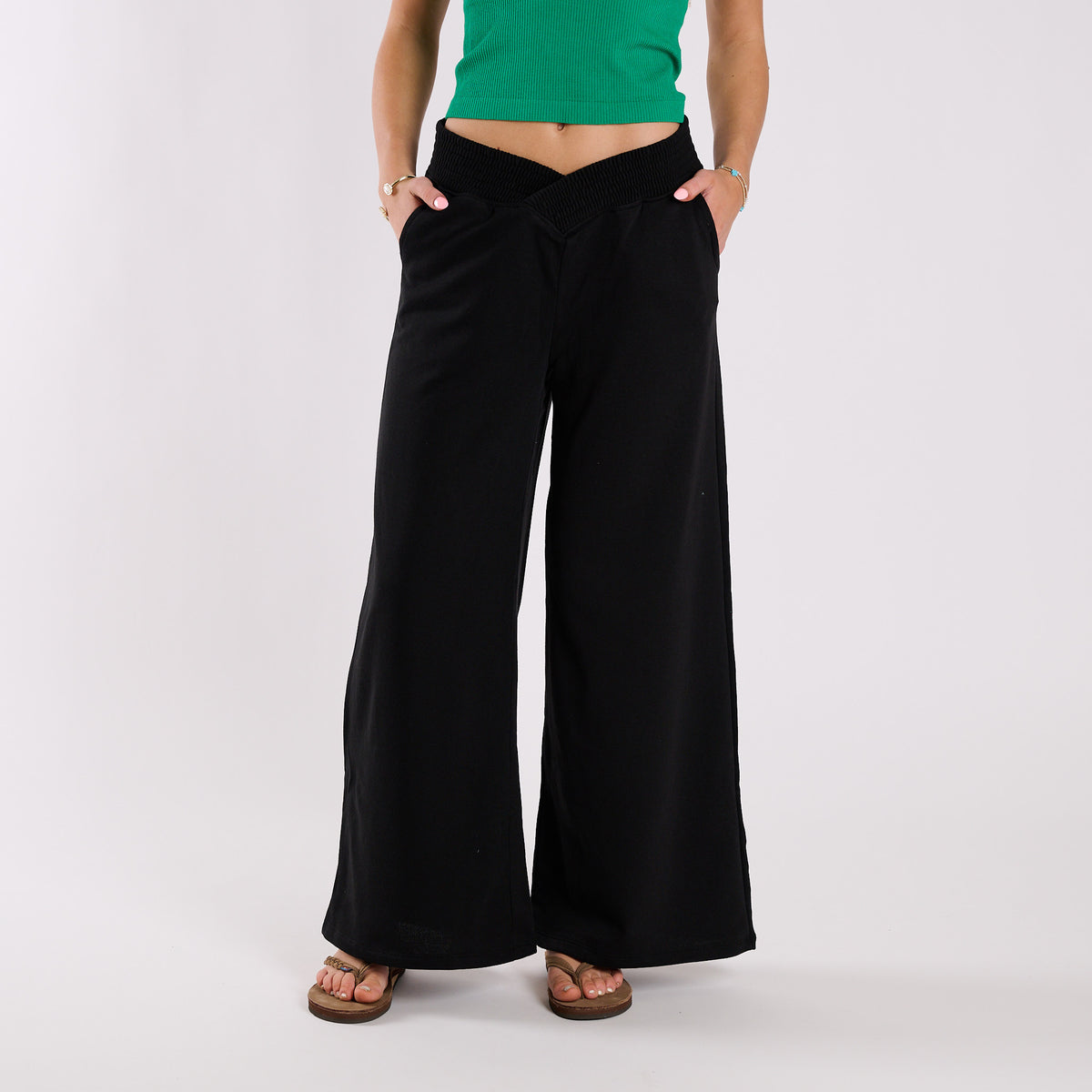 Person wearing black wide-leg pants and a green top on a white background
