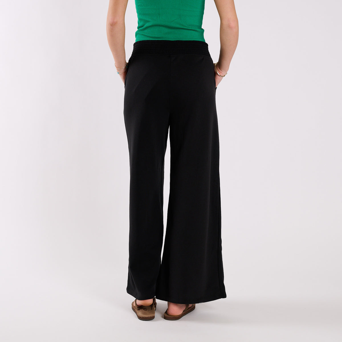 Person wearing black wide-leg pants and a green top on a white background